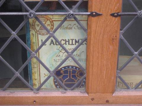 Buchcover von L'Alchimiste hinter einer vergitterten Fensterscheibe